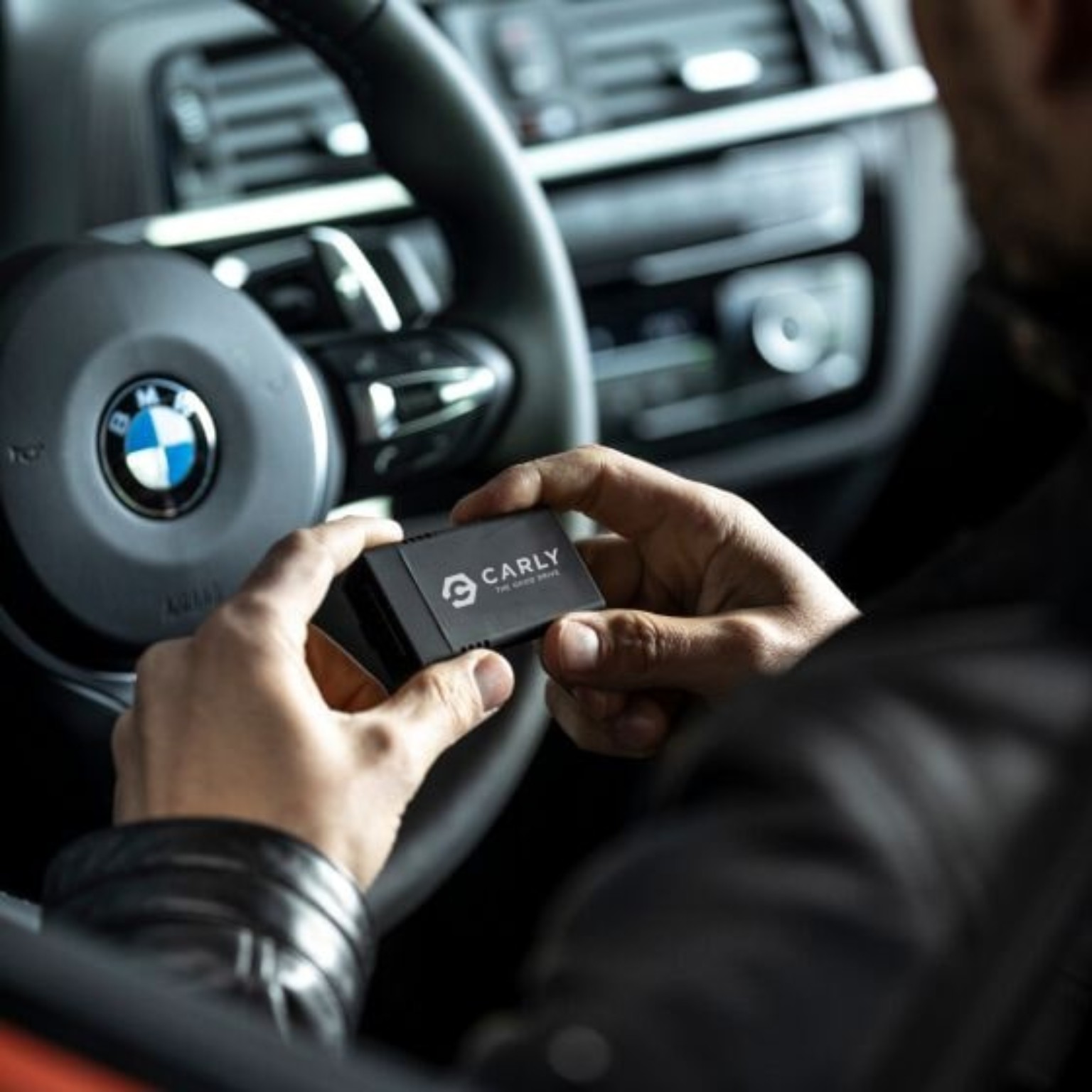 Person holding a Carly scanner in a parked vehicle